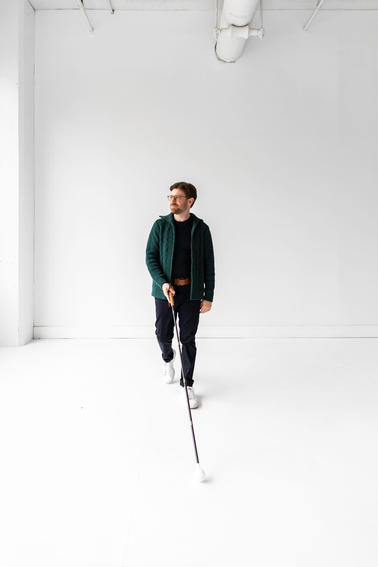 Charlie standing in a bright studio space, holding a white cane, wearing a green cardigan.